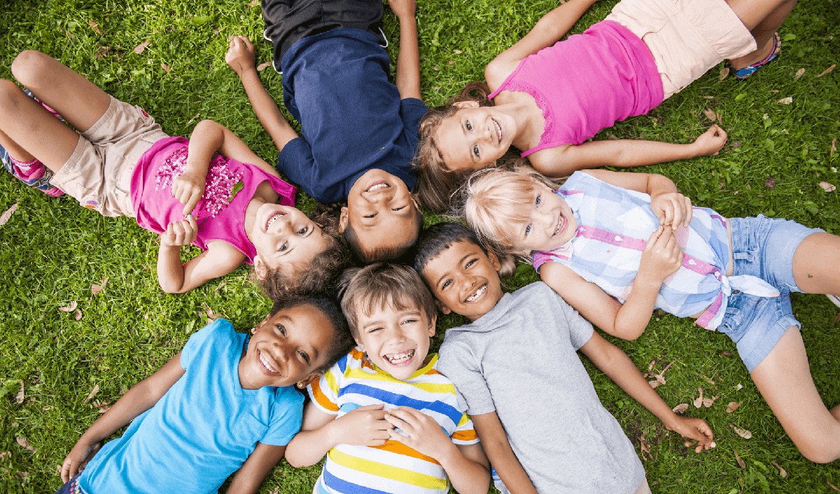 Smiling children lying on the grass, Child Neurology Consultants of Austin